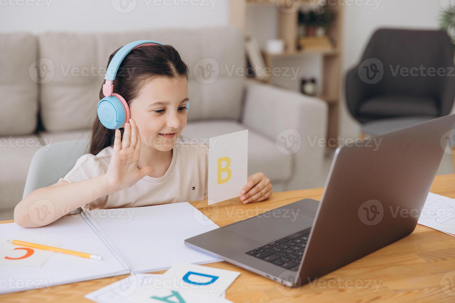 Smiling small girl in headphones watch lesson on computer with alphabet, happy little child in earphones have online web class using laptop at home, homeschooling concept photo