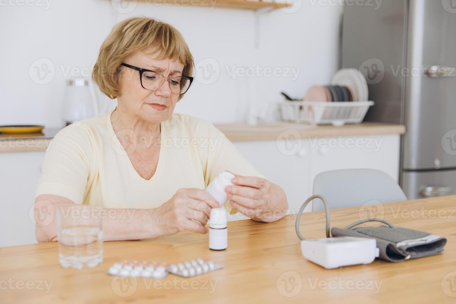 Elderly woman measuring blood pressure looking for pills and reading instructions in the kitchen at home photo