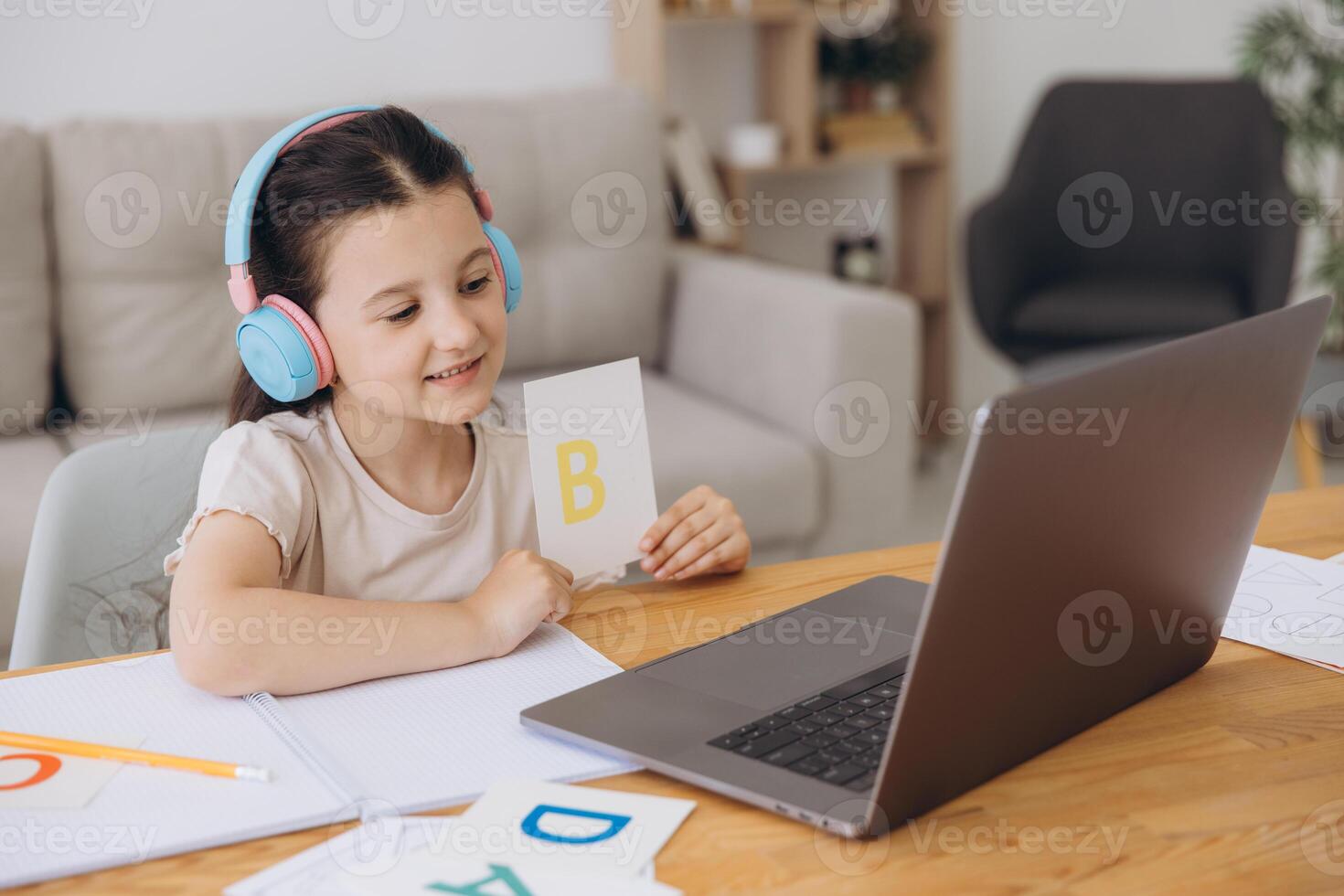 Smiling small girl in headphones watch lesson on computer with alphabet, happy little child in earphones have online web class using laptop at home, homeschooling concept photo