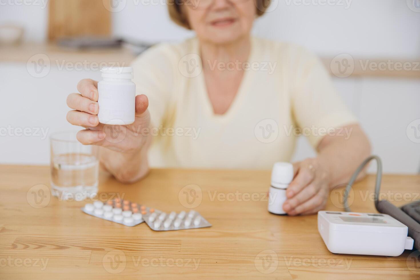 Elderly woman measuring blood pressure showing white pill jar mockup for your logo photo