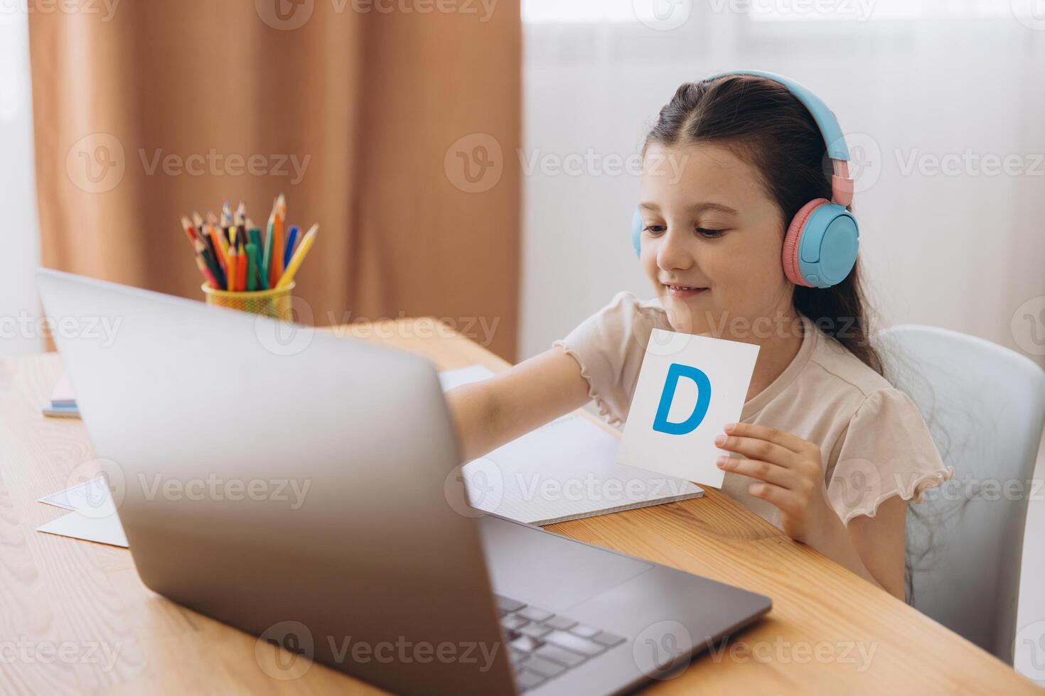 Smiling small girl in headphones watch lesson on computer with alphabet, happy little child in earphones have online web class using laptop at home, homeschooling concept photo