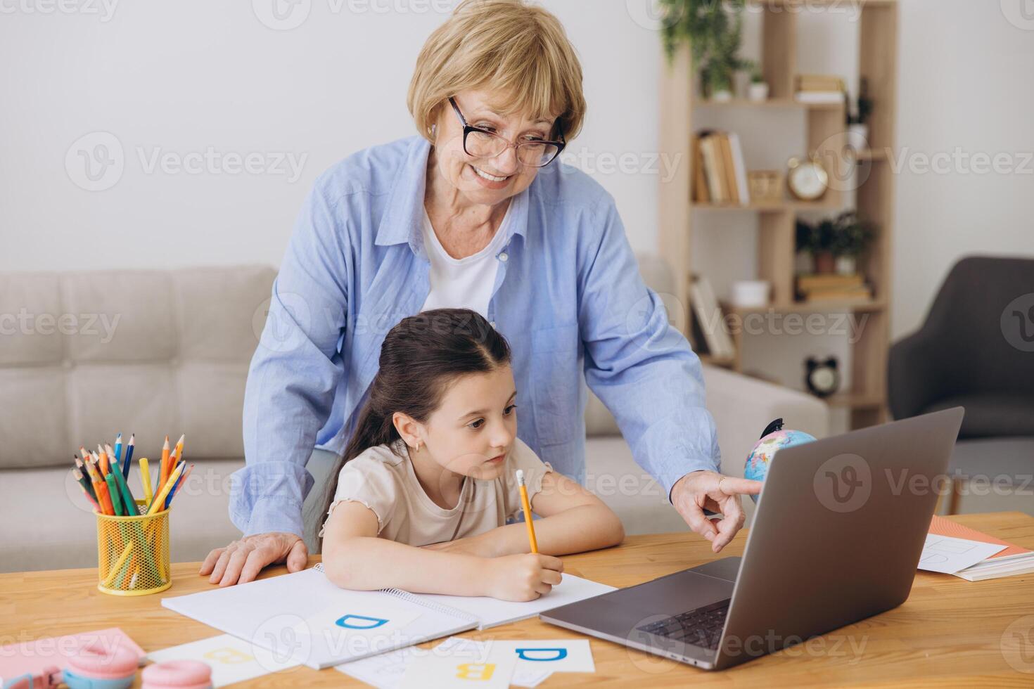 Happy grandma helping adorable preschool granddaughter school kid with homework task. Positive school pupil girl and granny reading learning book at laptop together, enjoying education at home photo