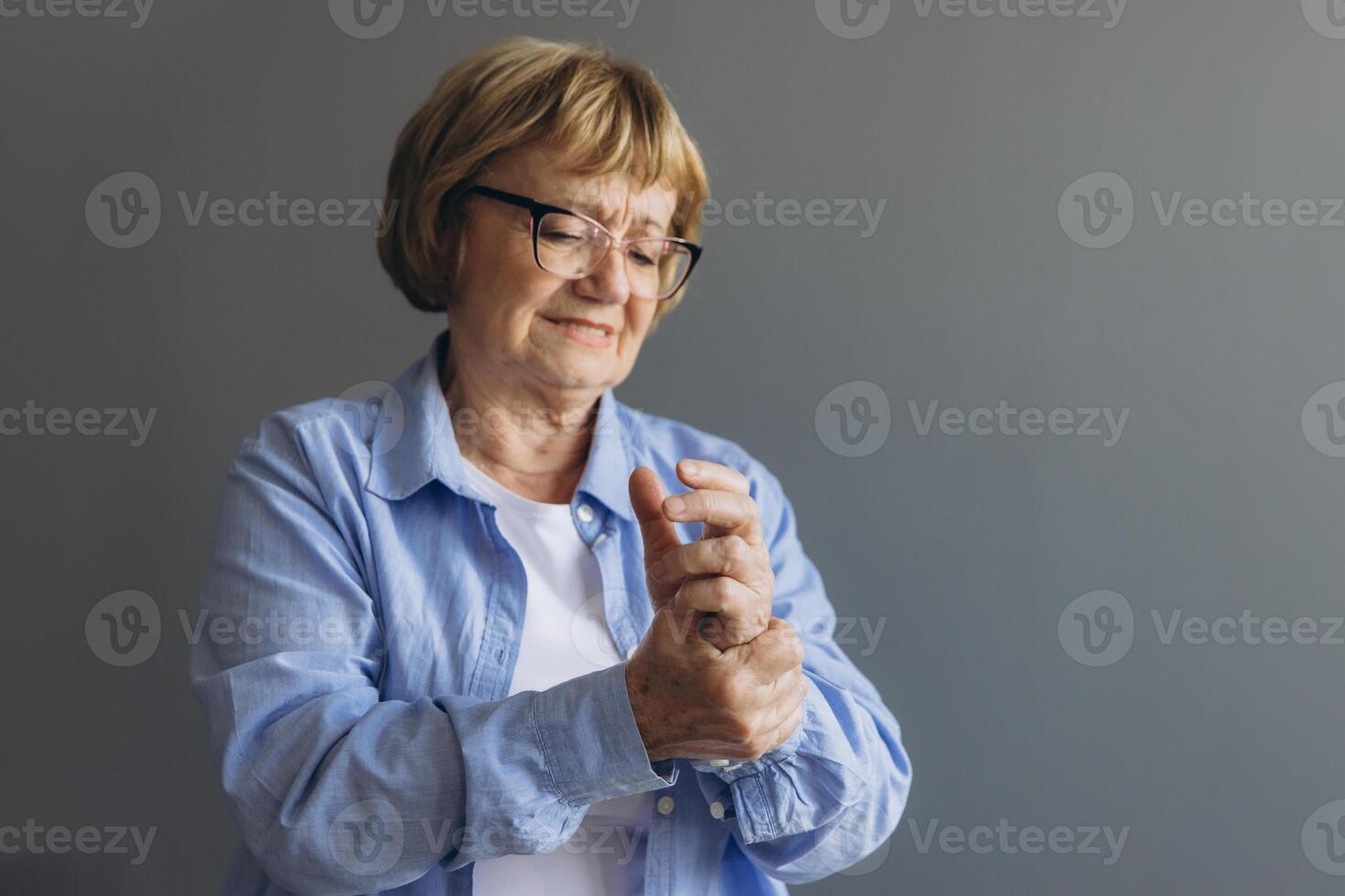 Elderly woman suffering from pain in hand, close up on gray background photo