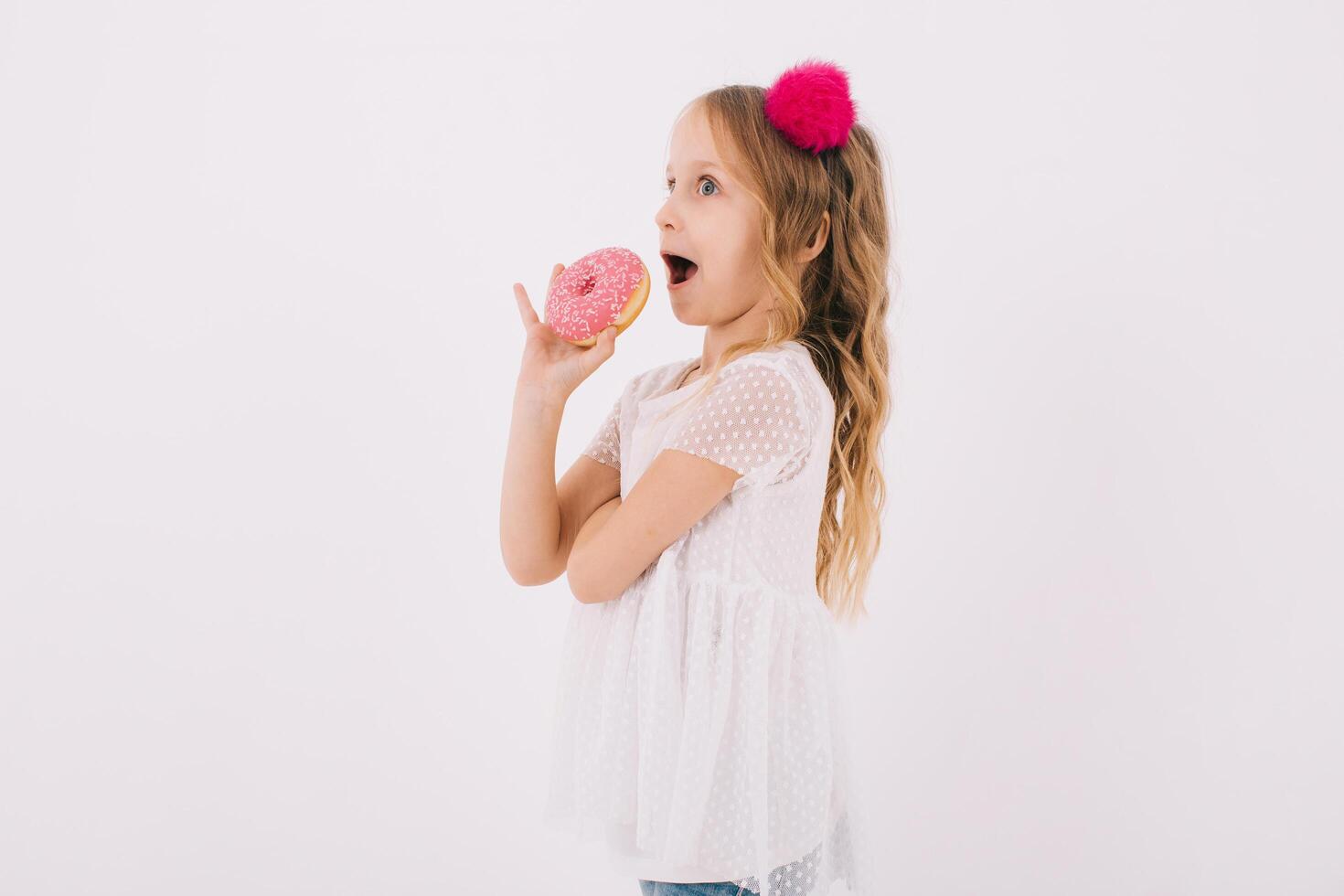 Funny little girl eating a donut on a white background photo