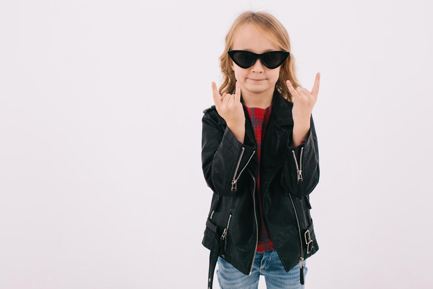 Funny little girl in leather jacket and sunglasses listening to rock music and showing fingers photo