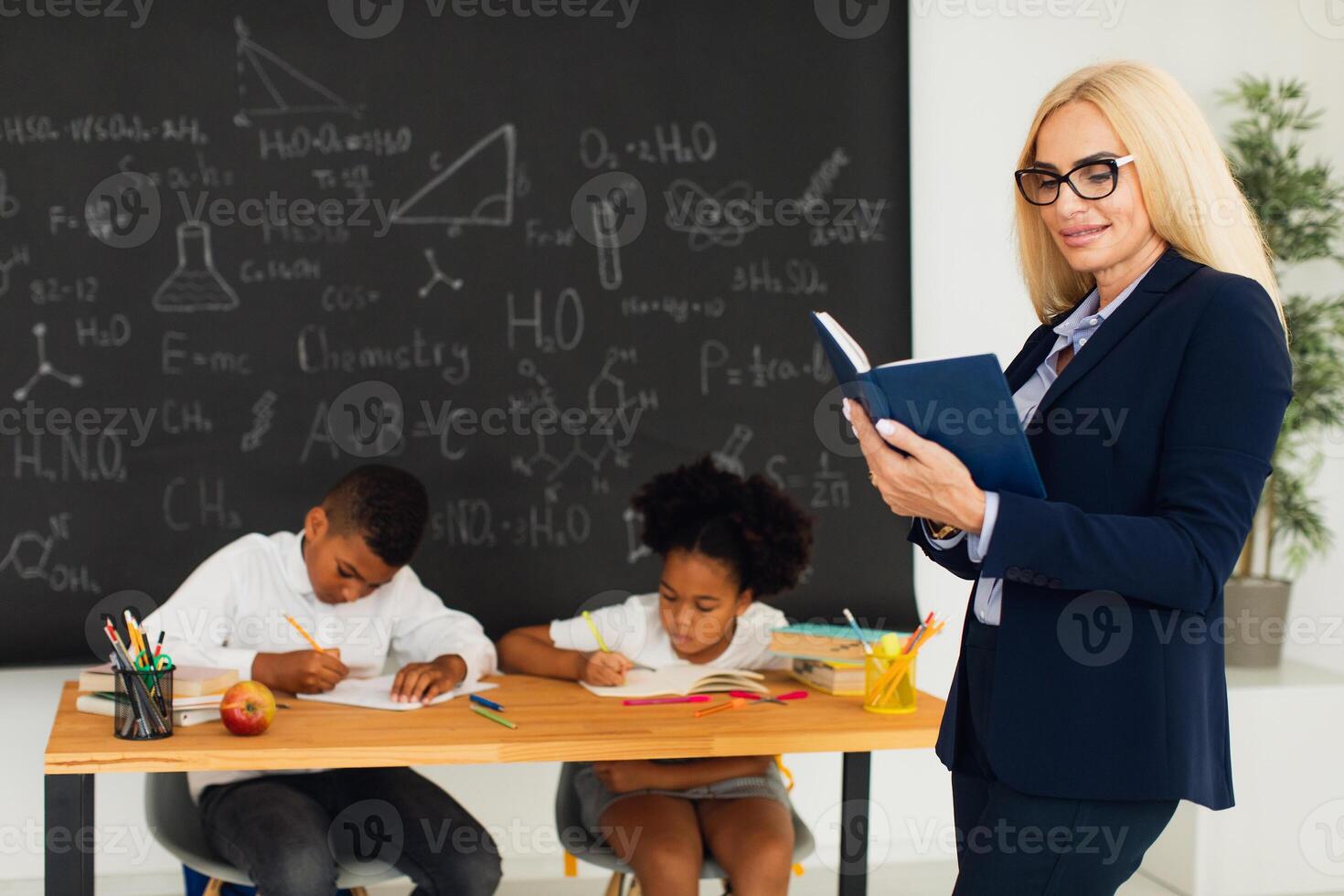 Portrait of female teacher standing on the background of a classroom and school children. photo