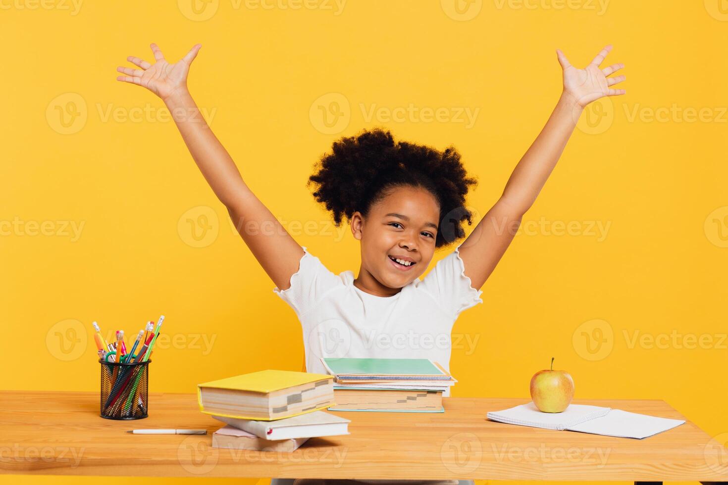 Happy African American female schoolgirl sitting at desk and stretching arm up during class. Back to school concept. photo