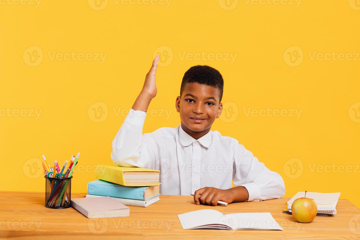 Happy African schoolboy sitting at desk and stretching arm up during class. Back to school concept. photo