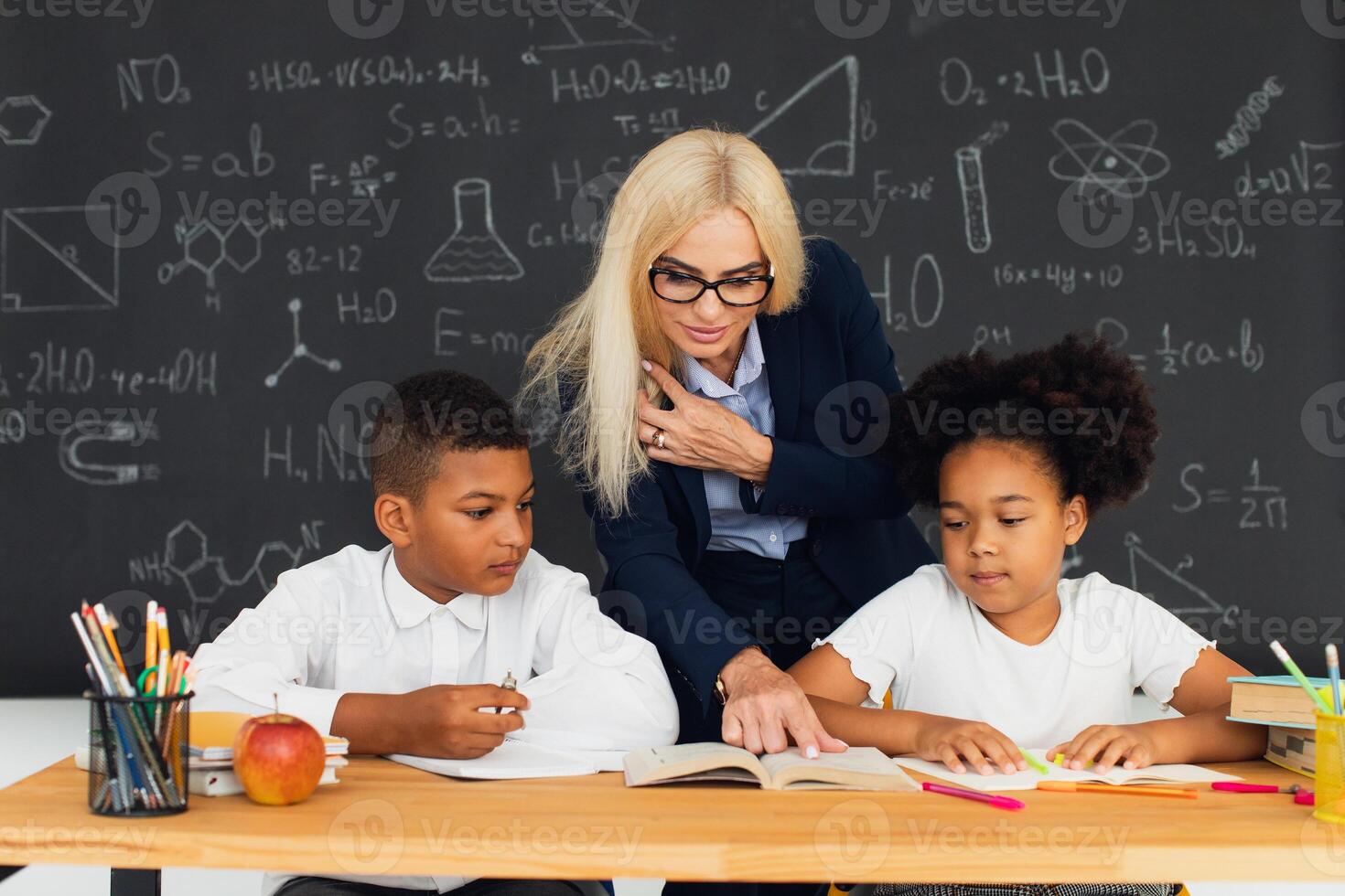 A female teacher teaches school children who sitting at a desk and solving problems. International team. Back to school. photo