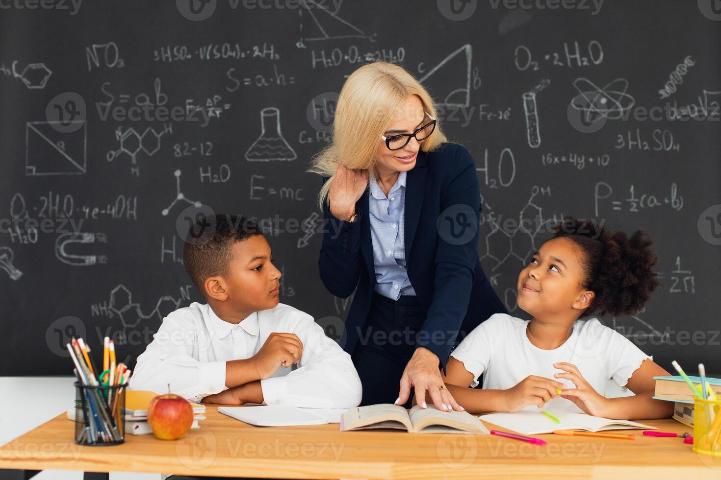 A female teacher teaches school children who sitting at a desk and solving problems. International team. Back to school. photo