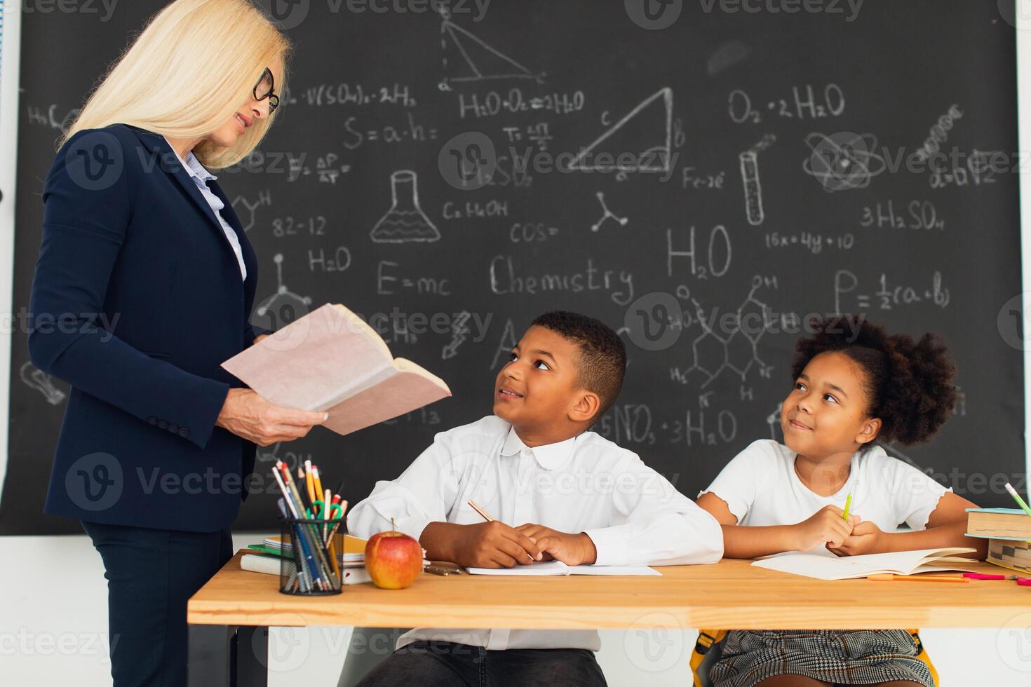 A female teacher teaches school children who sitting at a desk and solving problems. International team. Back to school. photo