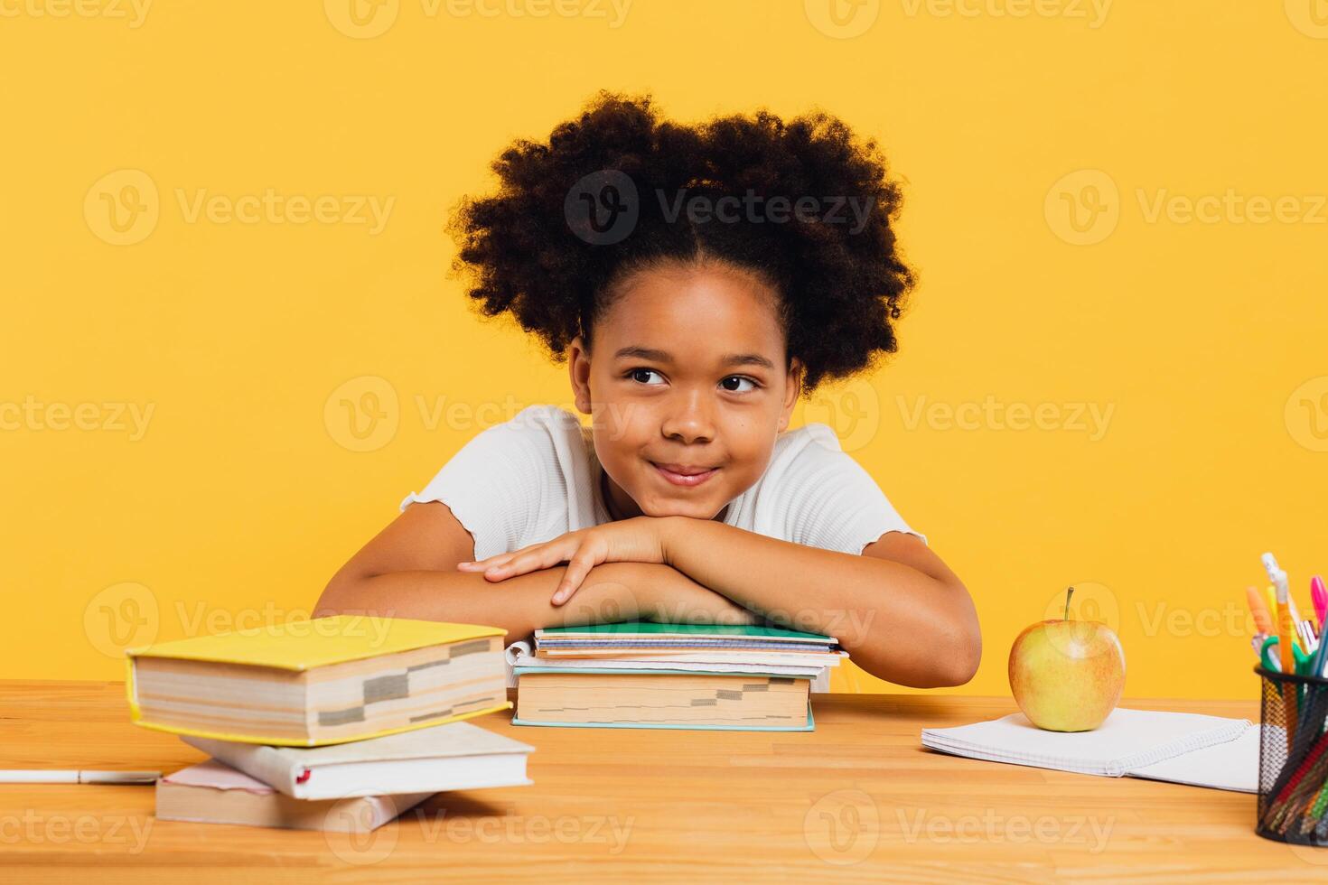 Happy African American schoolgirl sitting at desk leaning on books. Back to school concept. photo