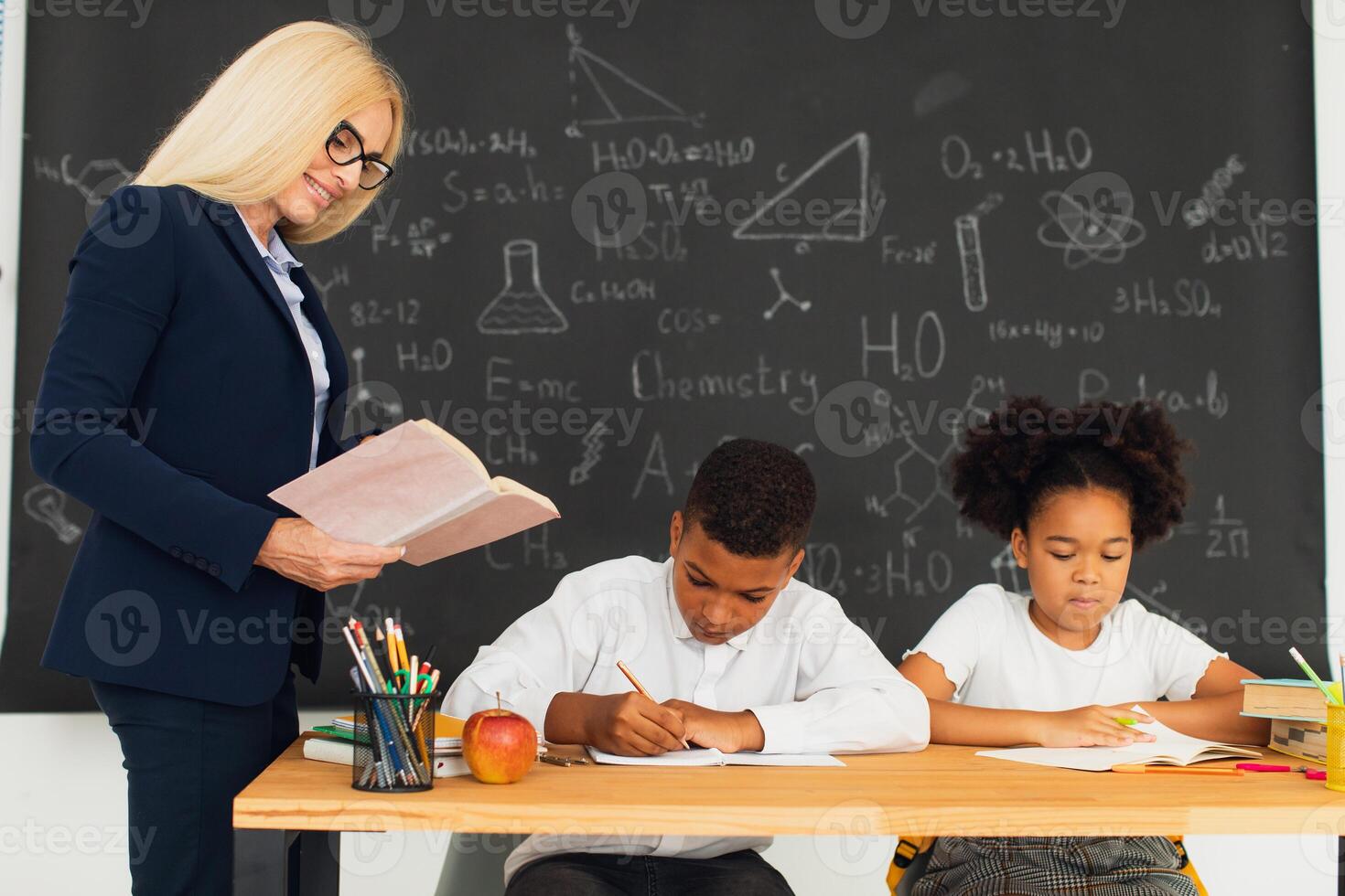 A female teacher teaches school children who sitting at a desk and solving problems. International team. Back to school. photo