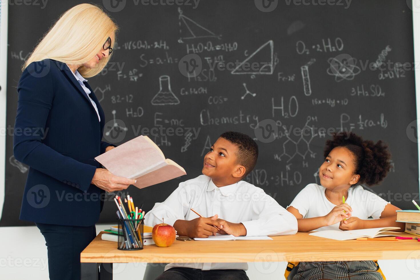 A female teacher teaches school children who sitting at a desk and solving problems. International team. Back to school. photo