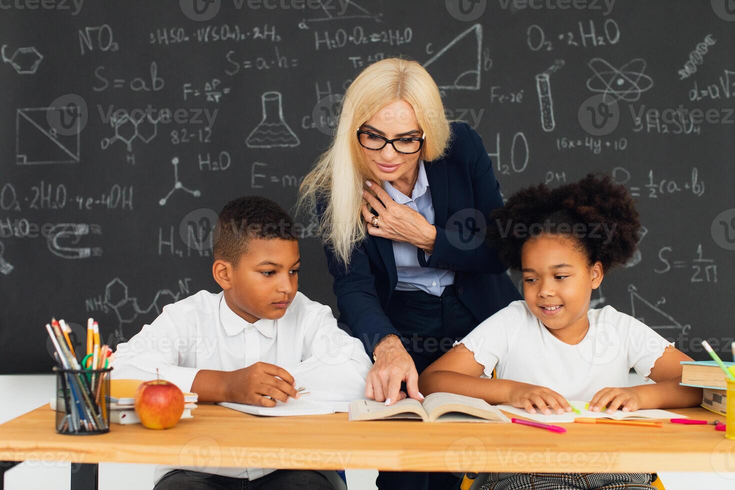A female teacher teaches school children who sitting at a desk and solving problems. International team. Back to school. photo