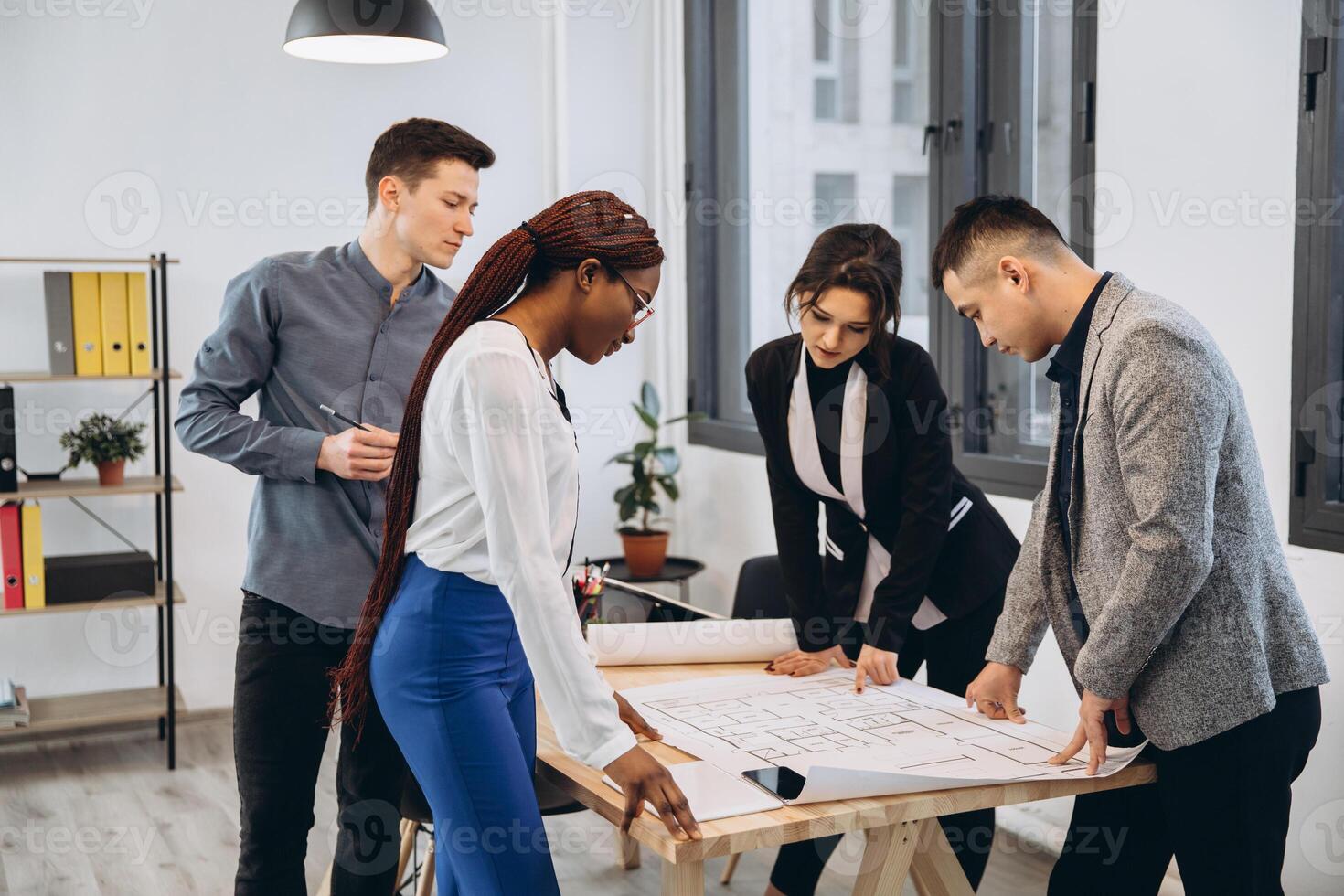 Group of young male and female students sharing ideas while working on project correcting mistakes in architectural drawings without using technologies collaborating in coworking space with bid desk photo