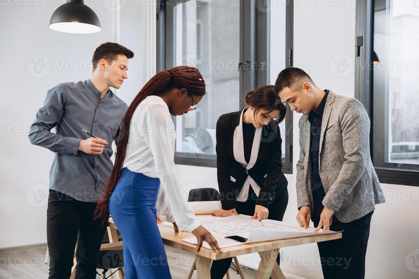 Group of young male and female students sharing ideas while working on project correcting mistakes in architectural drawings without using technologies collaborating in coworking space with bid desk photo