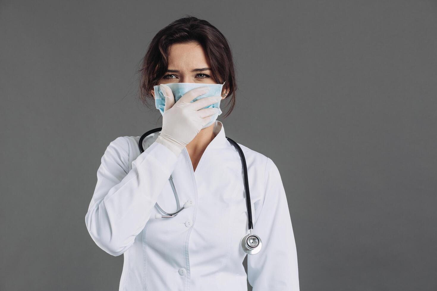 A gloomy and bewildered woman doctor with a stethoscope holds a mask. photo