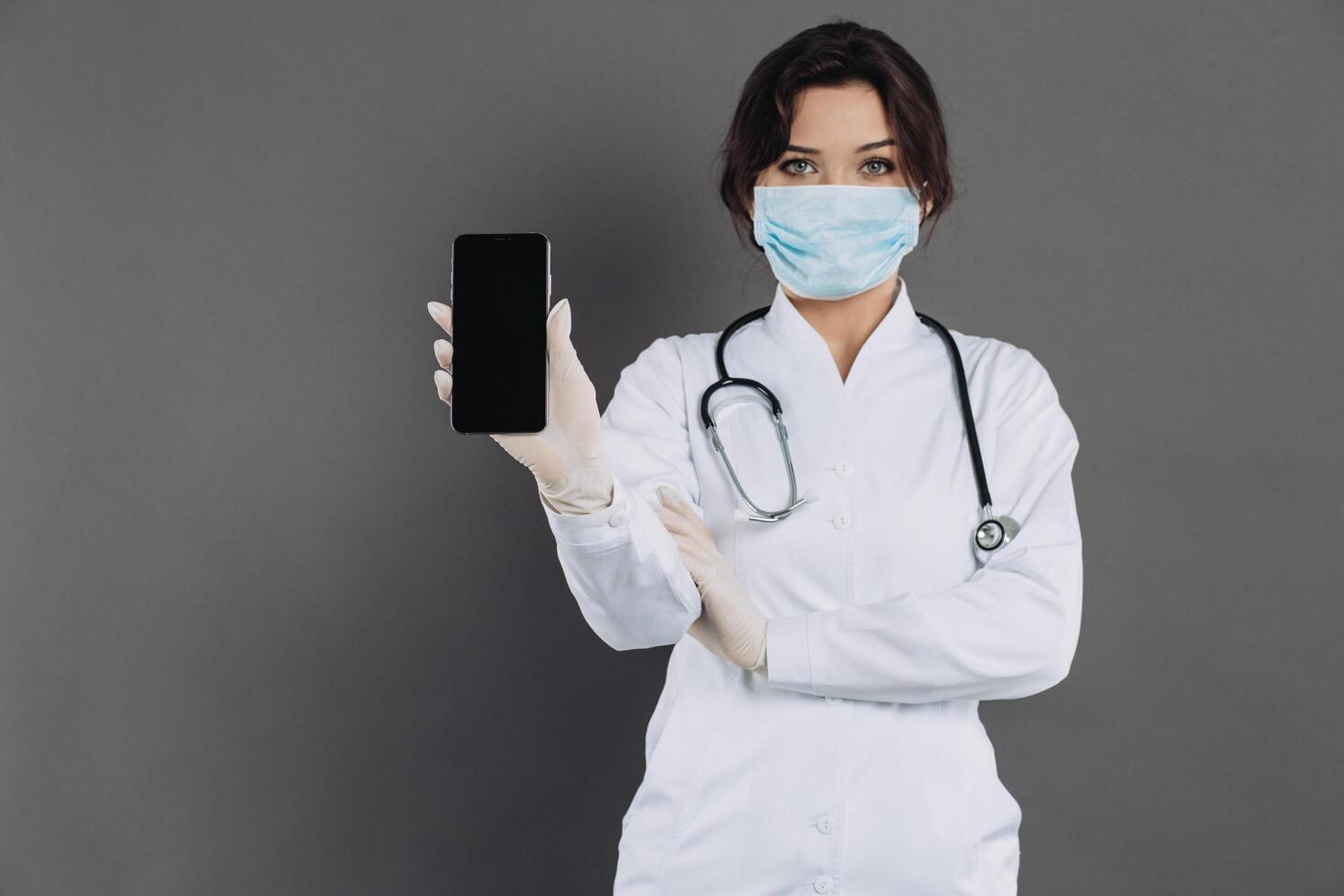 Female doctor wearing a stethoscope mask holding a smartphone and showing something. photo