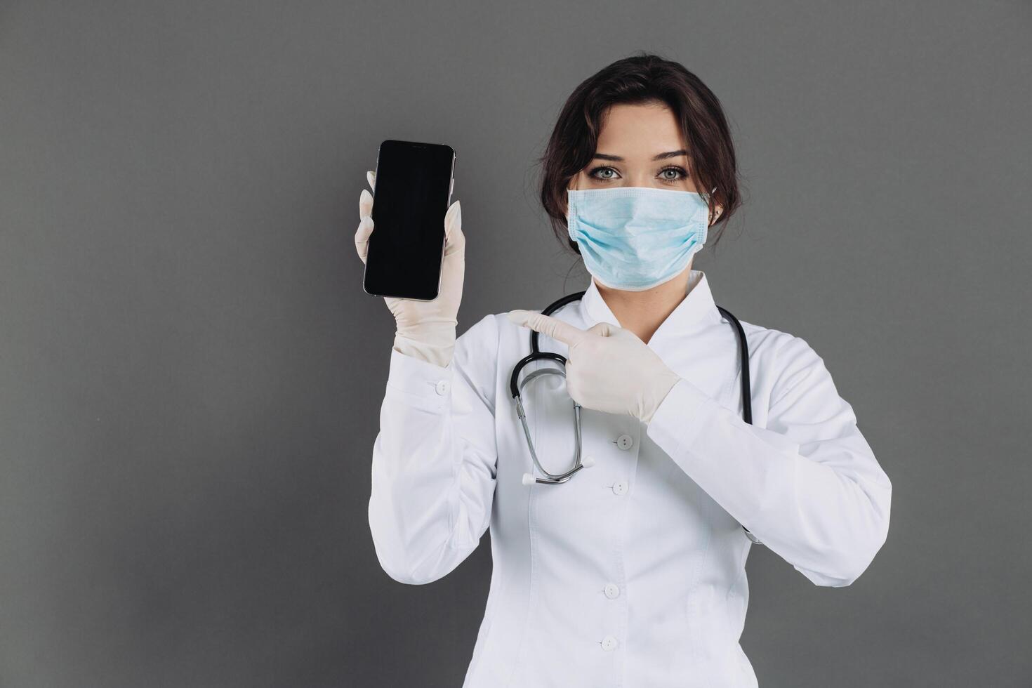 Female doctor wearing a stethoscope mask holding a smartphone and showing something. photo