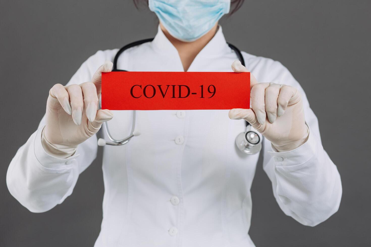 Doctor woman with surgical mask pointing to red paper with mesaage Coronavirus, isolated on gray background photo