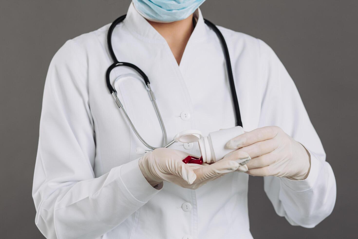 Doctor wearing mask and statoscope holding red antiviral pills against coronavirus. photo