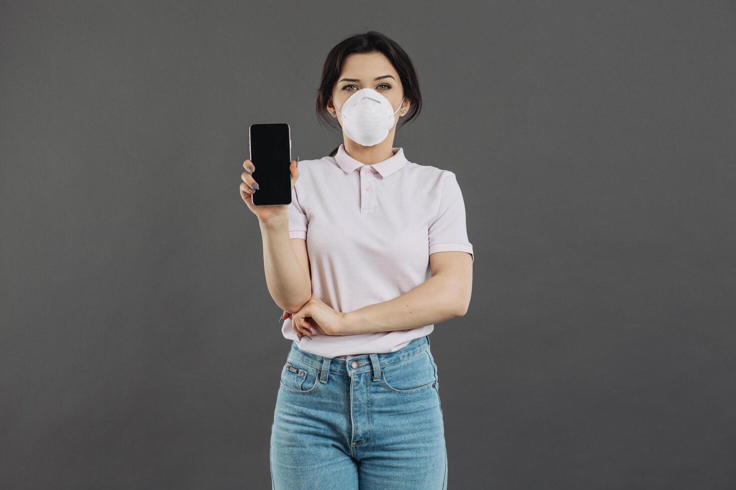 Woman in protective respiratory holding phone and showing something. Coronavirus concept and counteraction. photo