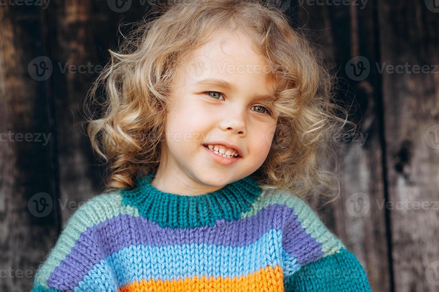 Portrait of a beautiful and happy curly girl in a knitted sweater near a wooden wall photo