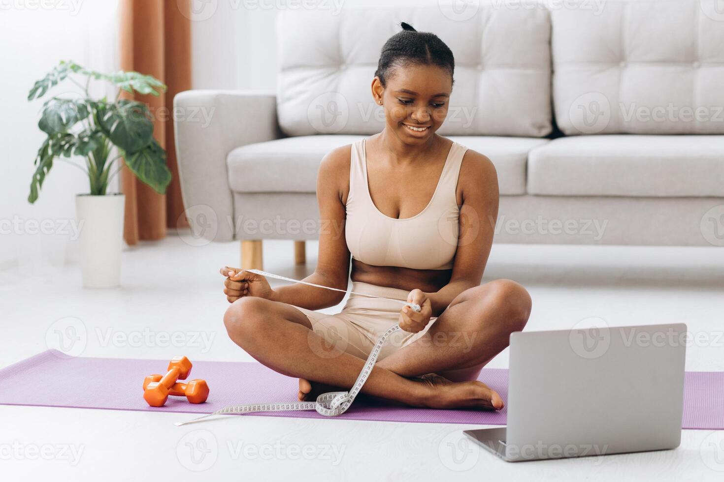 Young black woman measures her waist on the living room background. The concept of diet and weight loss. photo