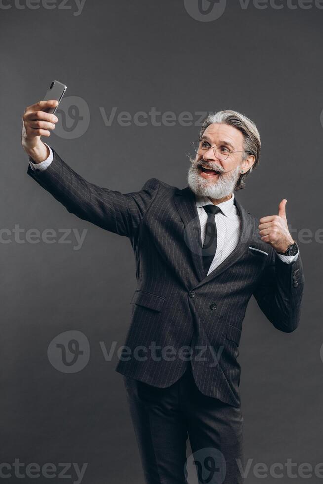 Business and fashionable bearded mature man in a gray suit make selfie on the grey background. photo