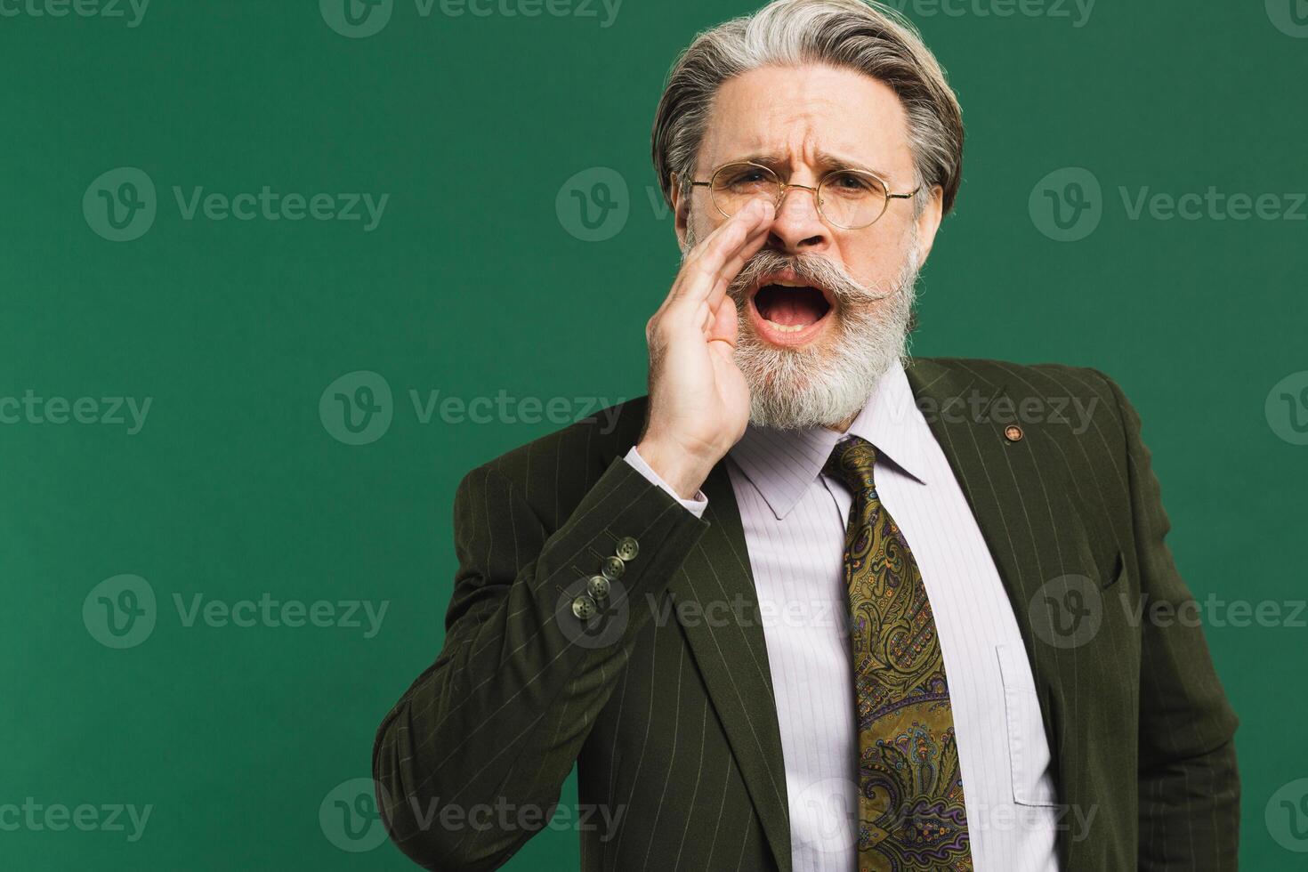 A bearded middle-aged teacher in a khaki suit shouts loudly against a on a green background photo