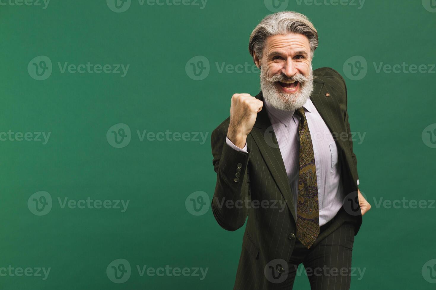 A middle-aged bearded man in a khaki suit screams loudly and holds his fist of happiness against a green background. Stock and win concept photo