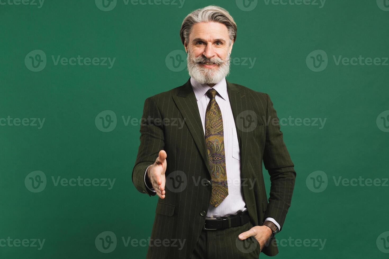 Middle-aged bearded man in khaki suit hand greetings on green background photo