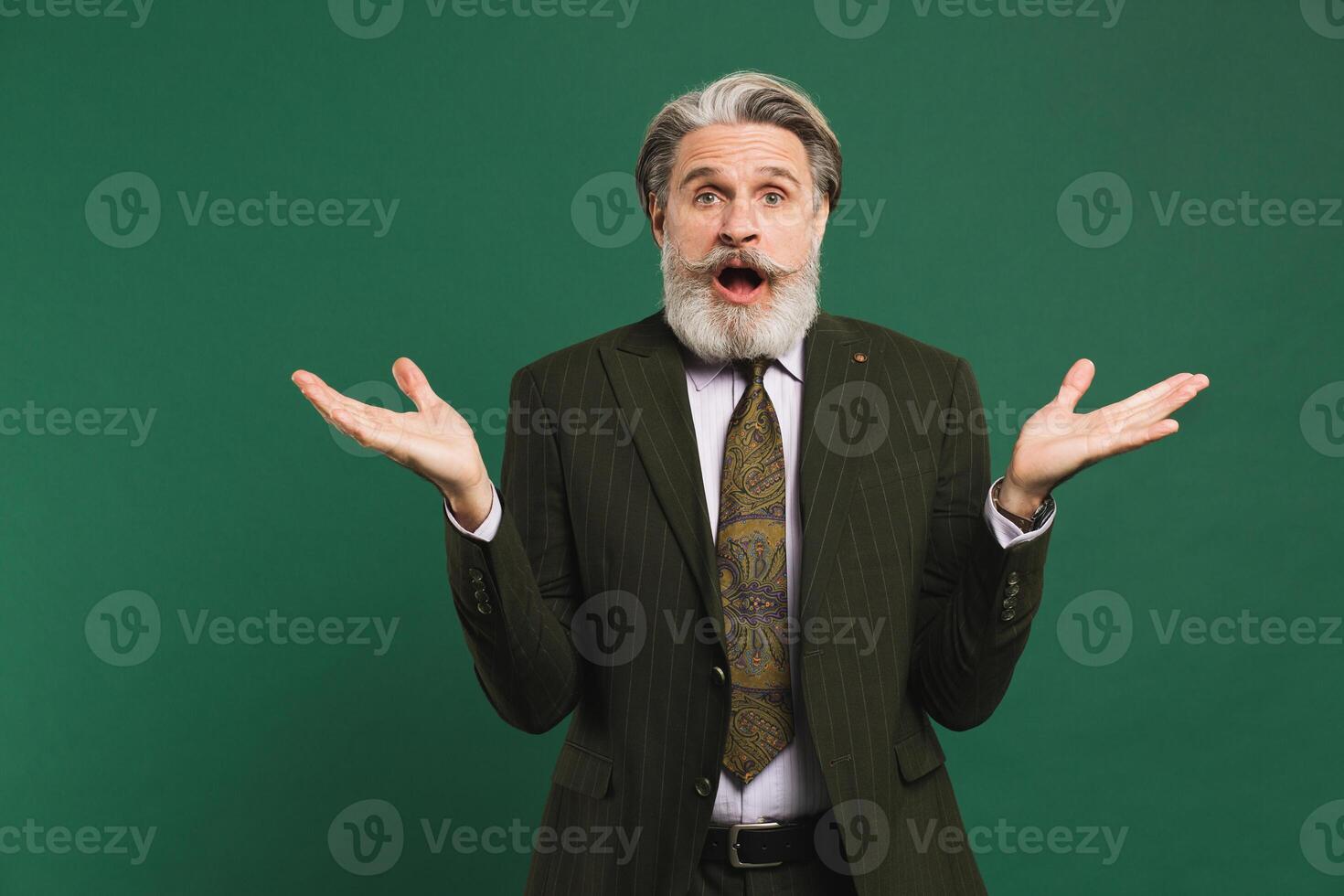 Bearded middle-aged man in khaki suit waving his hands to the side on a green background with copy space. photo