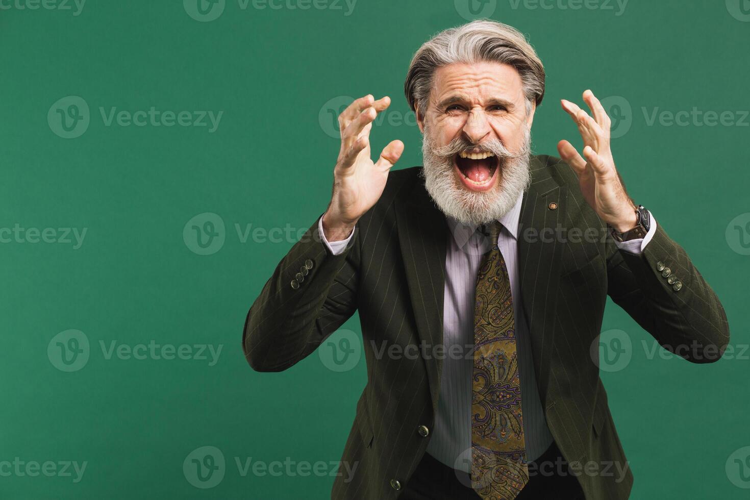 A middle-aged bearded man in a khaki suit shouts loudly and holds his fists against on a green background photo