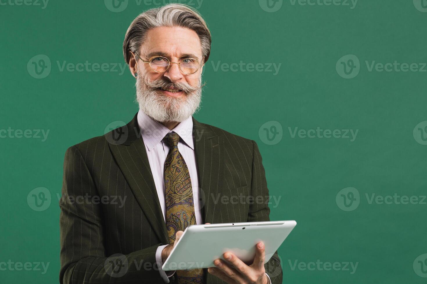 Middle-aged business man with beard and mustache in khaki suit holding tablet on green background photo