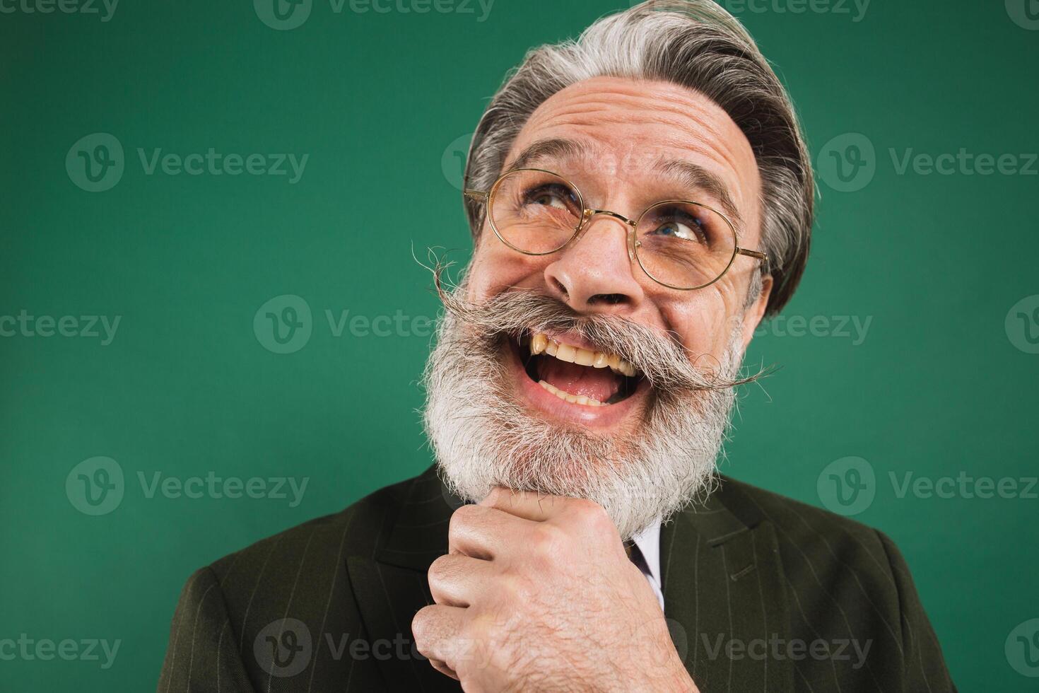 Bearded and funny teacher thinking and looking up, holding beard on green background photo
