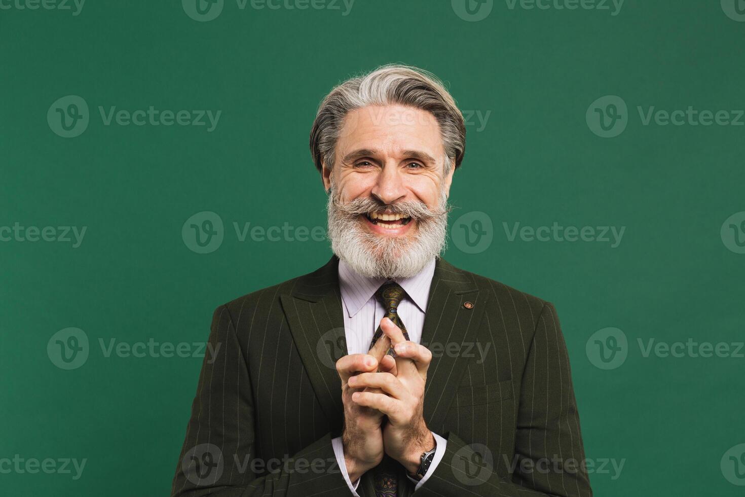 Bearded middle-aged man in suit crosses fingers for good luck and smiling on green background. photo
