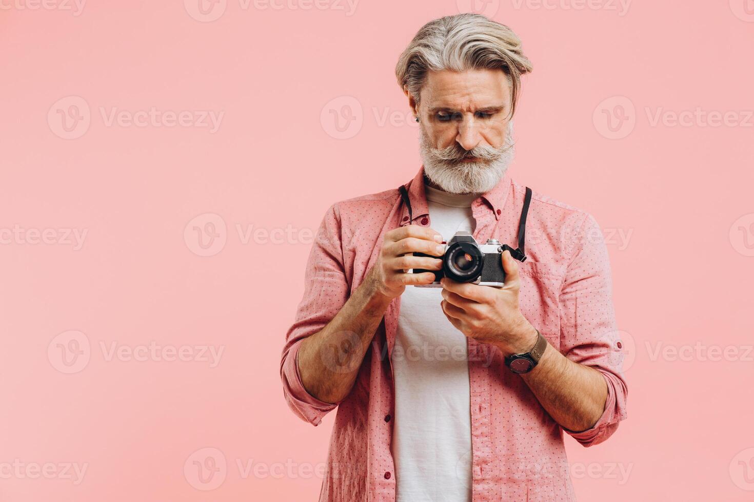 Middle-aged bearded photographer holding a camera on a pink background. photo