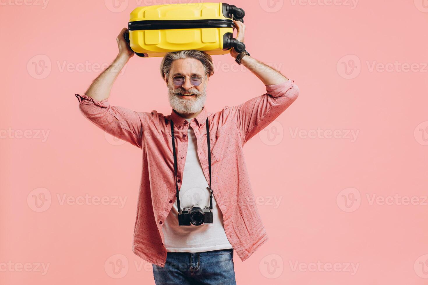 Stylish bearded man with a camera holds a yellow suitcase on a head photo