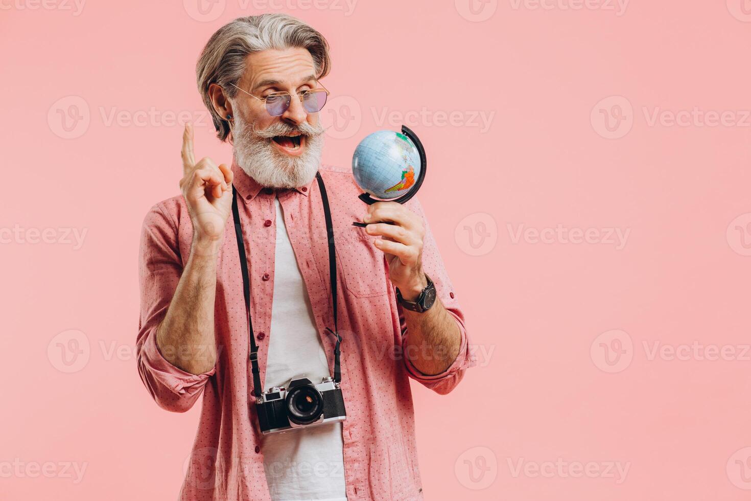 Happy bearded man in sunglasses with a camera chooses a country on a globe for travel. photo