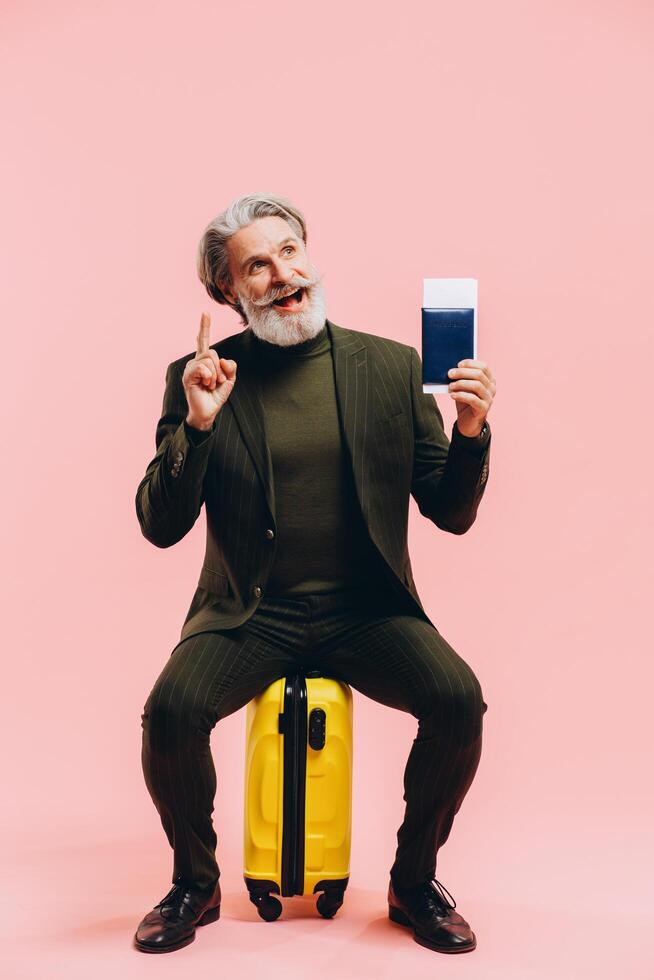 Stylish middle-aged man in a suit sits on a yellow suitcase and holds a passport. photo