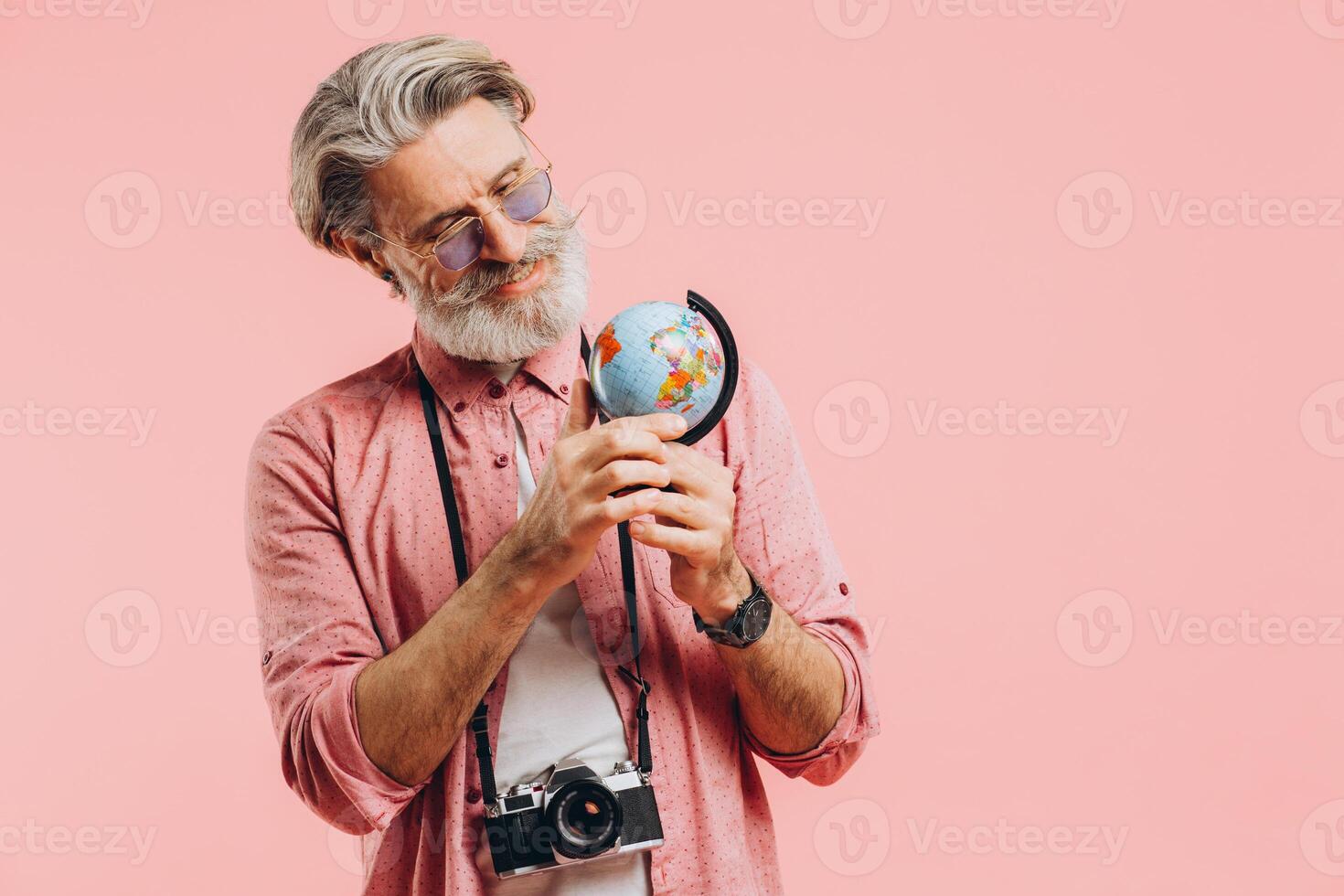 Happy bearded man in sunglasses with a camera chooses a country on a globe for travel. photo