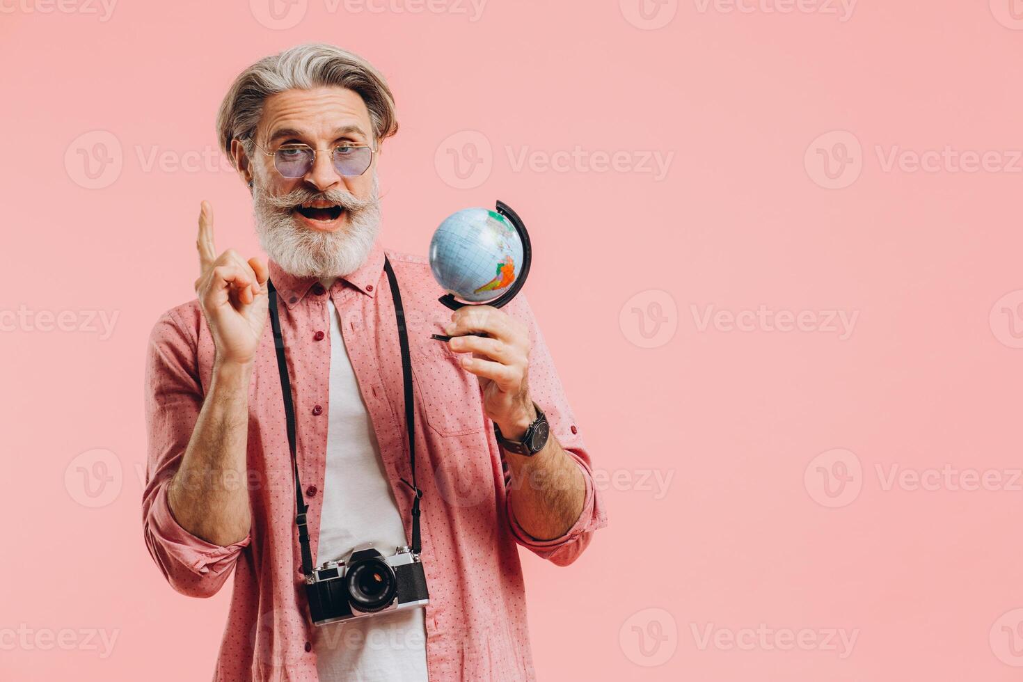 Happy bearded man in sunglasses with a camera chooses a country on a globe for travel. photo