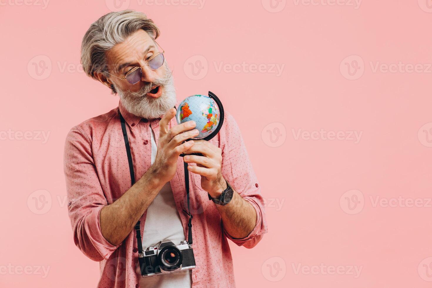 Happy bearded man in sunglasses with a camera chooses a country on a globe for travel. photo