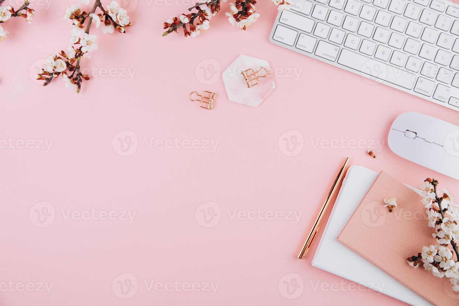 Spring flat lay top view home office workspace - modern keyboard and notebook with cherry blossom branches on a pink desk background photo