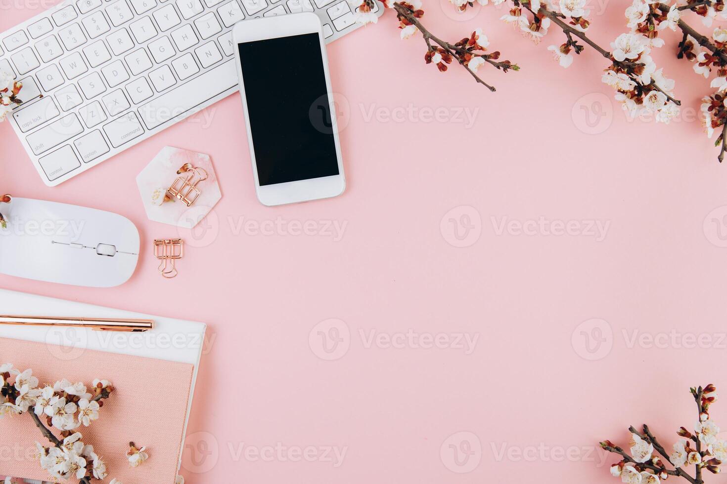Spring flat lay top view home office workspace - modern keyboard, smartphone and notebook with cherry blossom branches on a pink desk background photo