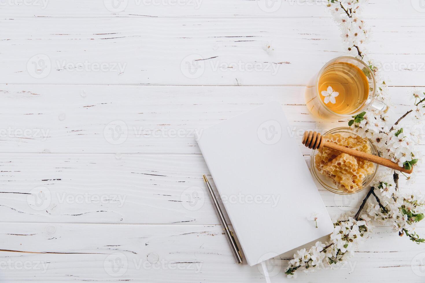 Spring composition. A cup of herbal tea, a jar of honey and cherry blossom near notebook on a white wooden background, top view. Place for text. Healthy food planning concept. photo