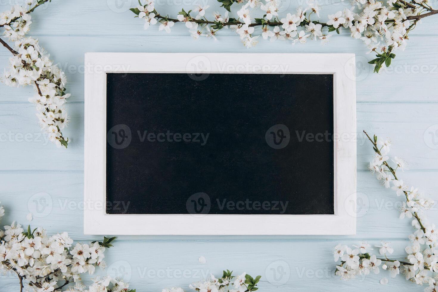 Spring flowers cherry blossoming around blackboard on the blue wooden background. Top view with copy space. Flat lay photo