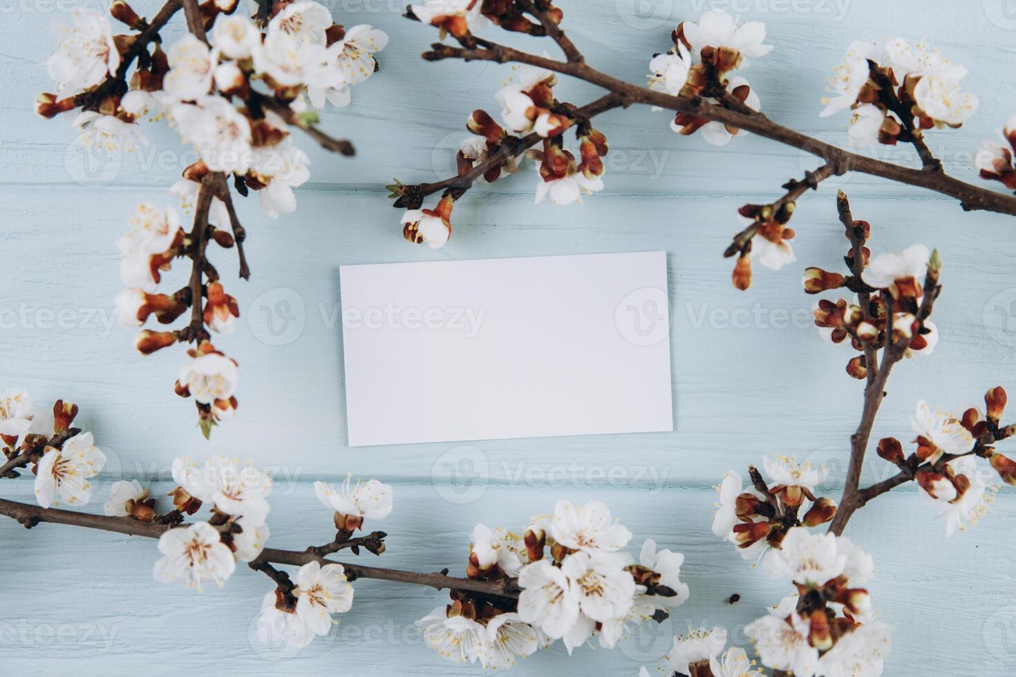 Spring flowers cherry blossoming around paper card on blue wooden background. Top view with copy space. Flat lay photo